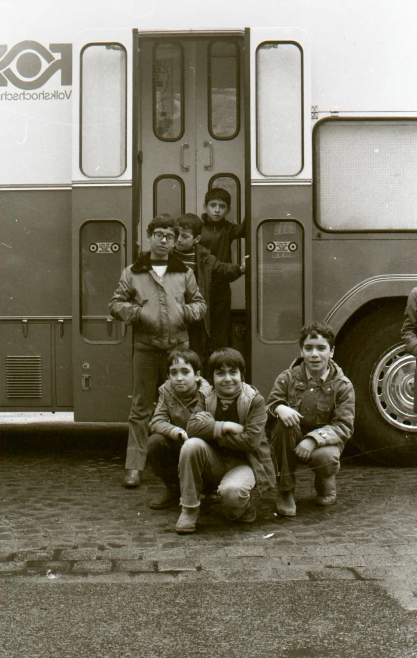 Kinder posieren vor der Tür des Bücherbusses der Stadtbibliothek. Auf der linken Seite erkennt man die Aufschrift Volkshochschule.