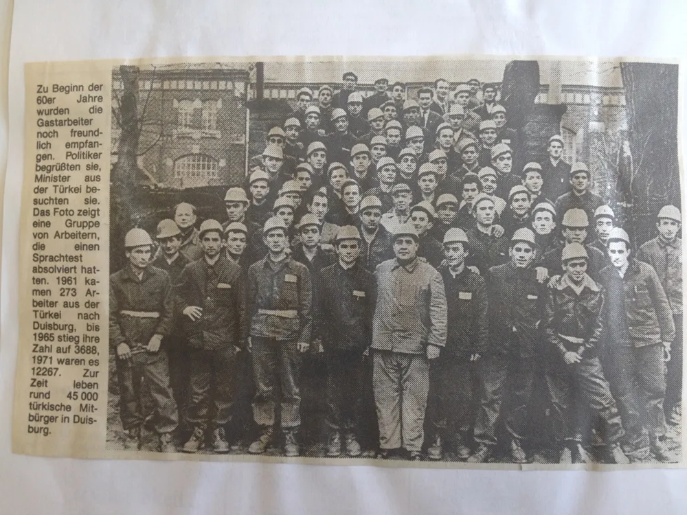Foto aus den frühen 1960ern von ca. 100 vor der Kamera posierenden Bergarbeitern mit Schutzhelmen aus der lokalen Zeitung.
